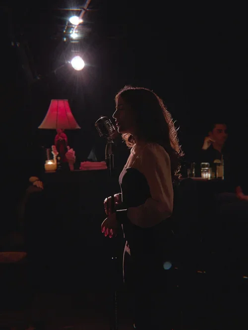 Emily singing into a vintage microphone on a dimly lit stage