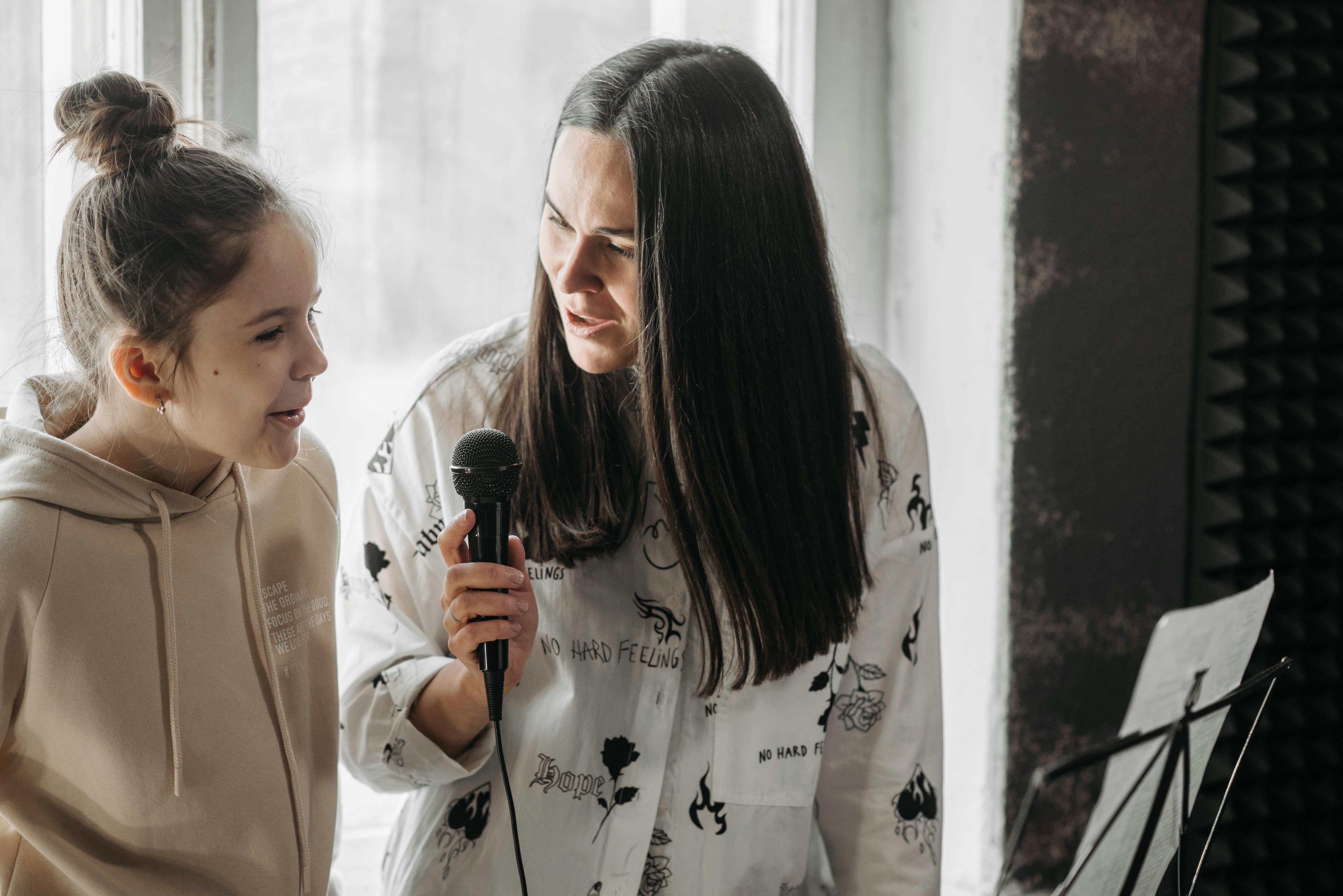 A voice teacher and young student singing together into a microphone